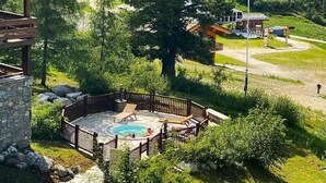 A hot tub area surrounded by a wooden deck, set against a backdrop of lush greenery and a mountainous landscape.