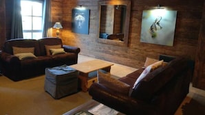 A cozy living room with a wooden ceiling, two leather sofas, a wooden coffee table, and a large mirror on the wall.