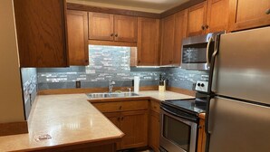 A kitchen with wooden cabinets, a stainless steel refrigerator, a stove, and a sink. - Lake view , Cozy One Bedroom! Walk to Beach and Town! (Bolton)