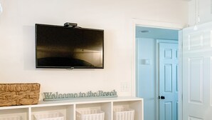 Un dormitorio con cama, televisor montado en la pared, estante con cestas y puerta que da a otra habitación.