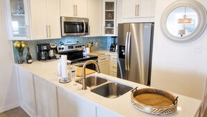 Una cocina moderna con armarios blancos, electrodomésticos de acero inoxidable, horno empotrado y un refrigerador grande.