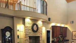 A spacious living room with a stone fireplace, a large clock, and a high ceiling with a balcony. - Splash in the Smokys ! (Sevierville)