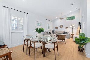 A modern living room with a glass dining table, two sofas, a ceiling fan, and a TV mounted on the wall. - Citrus Hideaway l Hot Tub l 1 Block to Downtown (St. Augustine)