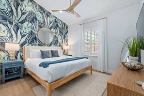 A bedroom with a bed, nightstands, a ceiling fan, a window with blinds, and a potted plant. - Citrus Hideaway l Hot Tub l 1 Block to Downtown (St. Augustine)