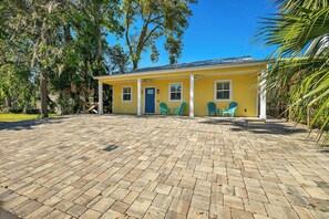 A yellow building with a covered porch, two windows, and a door. There are two green chairs outside.