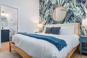 Un dormitorio con cama, espejo, mesita de noche y un muro con diseño de hojas.