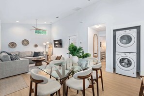 Un salon moderne avec une table à manger en verre, un canapé gris et un lave-linge en arrière-plan.