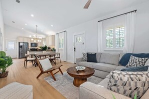 Una cocina moderna con comedor, una sala de estar con sofá y mesa de centro, y un gran ventanal con cortinas.