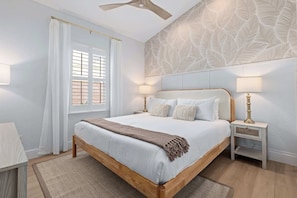 A bedroom with a bed, bedside tables, a window with curtains, a ceiling fan, and a patterned wall.