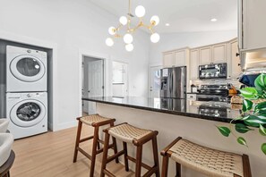 A modern kitchen with stainless steel appliances, a central island, and bar stools. - Citrus Hideaway l Hot Tub l 1 Block to Downtown (St. Augustine)