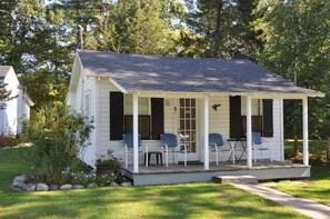 A small white house with a porch, two chairs, and a table. - Glen Cottage at Cozy Nook (Lake George)