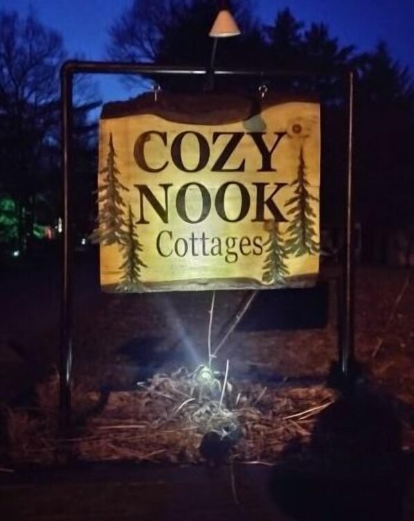 A sign for 'COZY NOOK Cottages' with a rustic design and a campfire illustration. - Glen Cottage at Cozy Nook (Lake George)