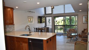 A modern kitchen with wooden cabinets, a dishwasher, and a dining area with a table and chairs. - Beautifully remodeled 2 Bd, 2 Bath Condo, short walk to the Beach (Kihei)