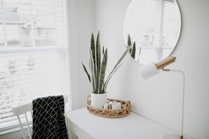 Habitación blanca con una planta en maceta, un espejo redondo y una lámpara de pie sobre una superficie blanca.