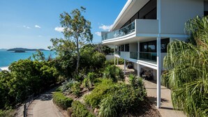 Une maison moderne à deux étages, dotée d’un balcon donnant sur une zone côtière.