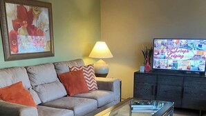 Una sala de estar con un sofá, una mesa de centro, una lámpara, un televisor y una silla.