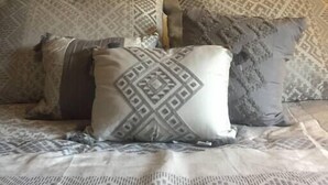 Una cama con ropa de cama y almohadas estampadas, una obra de arte enmarcada encima y un cabecero de madera.