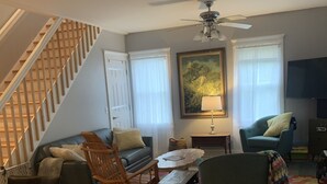Ein Wohnzimmer mit Treppe, Deckenventilator, Sofa, Couchtisch und Fernseher.