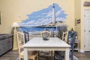 Een eetgedeelte met een tafel, stoelen, een lamp en een muurschildering van een vuurtoren.