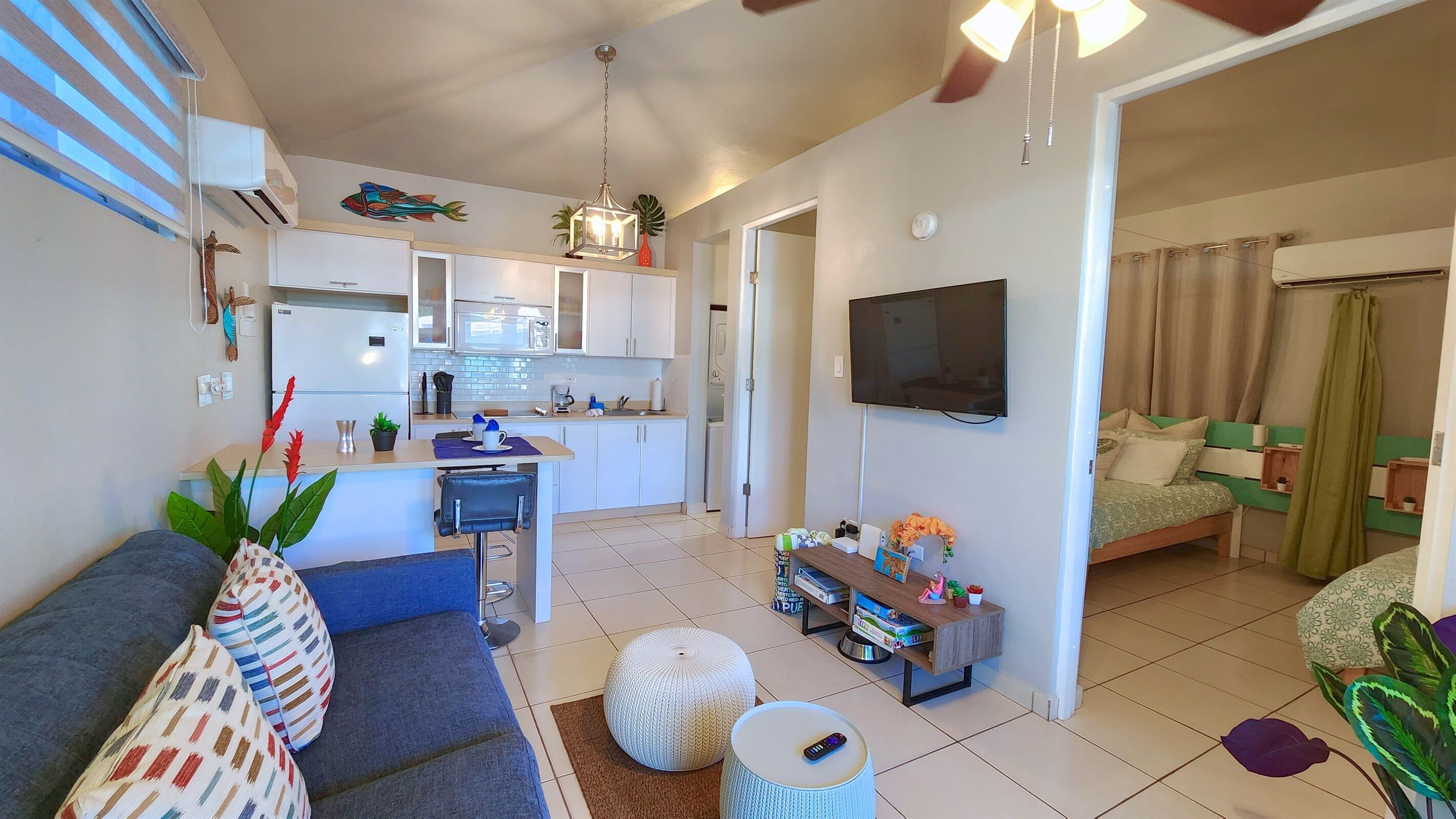 A modern apartment with a kitchen, living room, and bedroom. It includes a sofa, a dining table, and a TV.