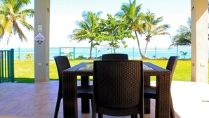 An outdoor patio with a table and chairs, palm trees, and a view of the ocean. - Casa Tortuga | Beachfront Villa | Pool | Aguada PR (Aguada)