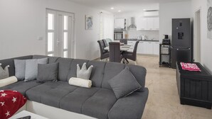 A modern living room with a grey sofa, a dining table with chairs, a kitchen area with white cabinets, and a black refrigerator. - Gorgeous home in Barban (Barban)