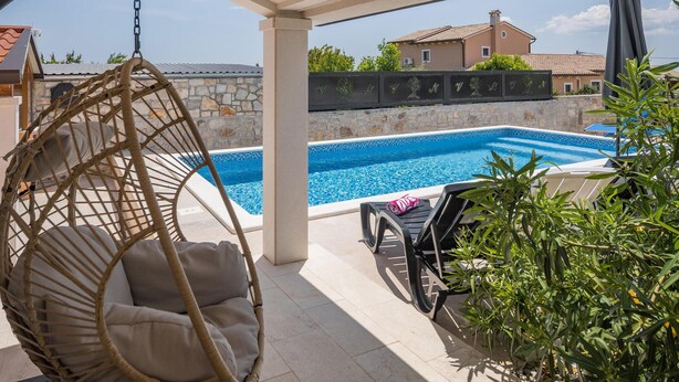 A pool area with a hanging chair, lounge chairs, and a stone wall. - Gorgeous home in Barban (Barban)