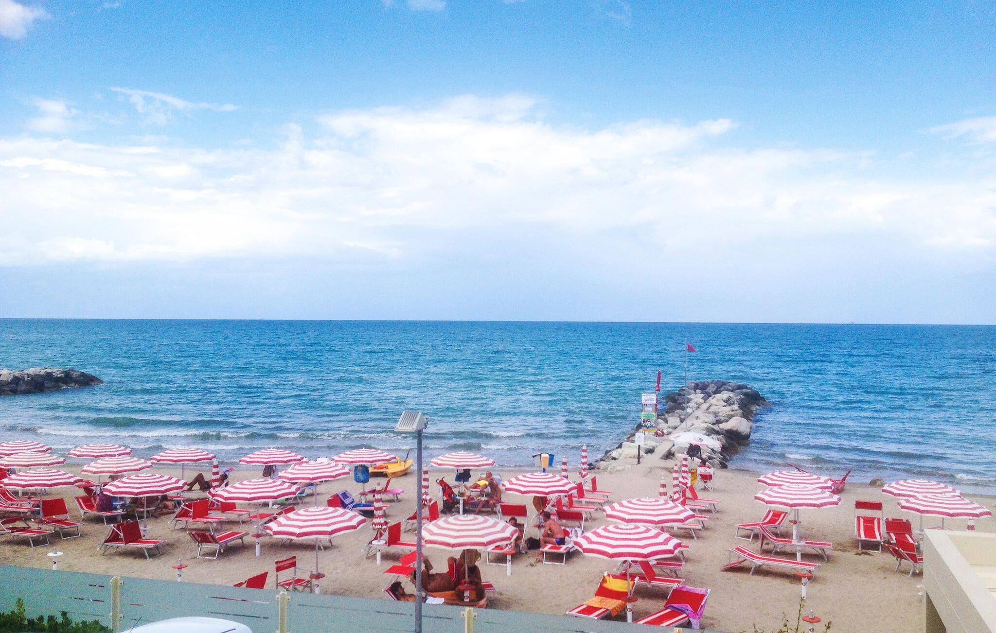 A beach with rows of red and white striped umbrellas and lounge chairs.