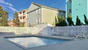 Une piscine rectangulaire entourée d’une clôture blanche et agrémentée de chaises longues.