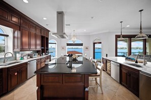 A spacious kitchen with a large island, dark wooden cabinets, and a view of the sea.