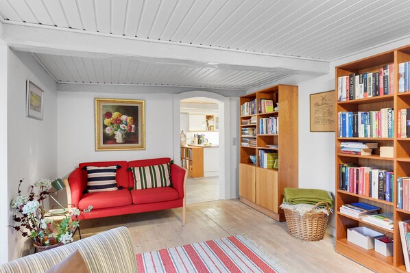 A cozy living room with a red sofa, a bookshelf filled with books, and a painting on the wall. - Awesome home in Haderslev with WiFi (Haderslev)