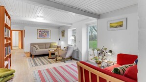 A spacious living room with a sofa, armchairs, a red chair, a coffee table, and a bookshelf.