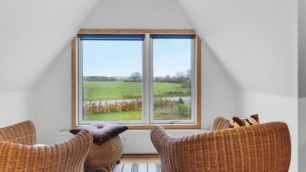 A room with a large window, wicker furniture, and a view of a green field.