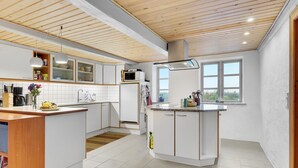 A modern kitchen with white cabinetry, a central island, and a large window providing natural light.