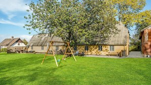 A house with a well-maintained lawn, a swing set, and a large tree providing shade.