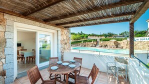 A covered patio with a pool, stone walls, and a dining area with wooden furniture. - Amazing apartment in Baja Sardinia (Baja Sardinia)
