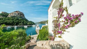 A coastal view with boats docked at a marina, a mountain in the background, and a white building with a staircase leading to an entrance. - Amazing apartment in Baja Sardinia (Baja Sardinia)
