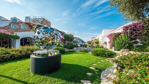 A garden with a reflective sculpture, white buildings, and a clear blue sky. - Amazing apartment in Baja Sardinia (Baja Sardinia)