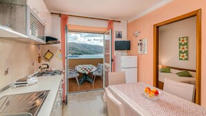 Une cuisine compacte comprenant un coin repas, un réfrigérateur et une table dressée pour deux personnes, avec un saladier de fruits.