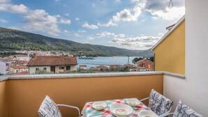 Un balcon avec une table dressée pour le dîner, offrant une vue sur une ville côtière et une étendue d’eau.