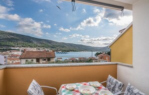 A balcony with a table set for dining, overlooking a coastal town and a body of water.