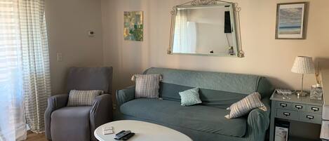 A living room with a grey armchair, a green sofa, a white coffee table, and a small side table with a lamp.