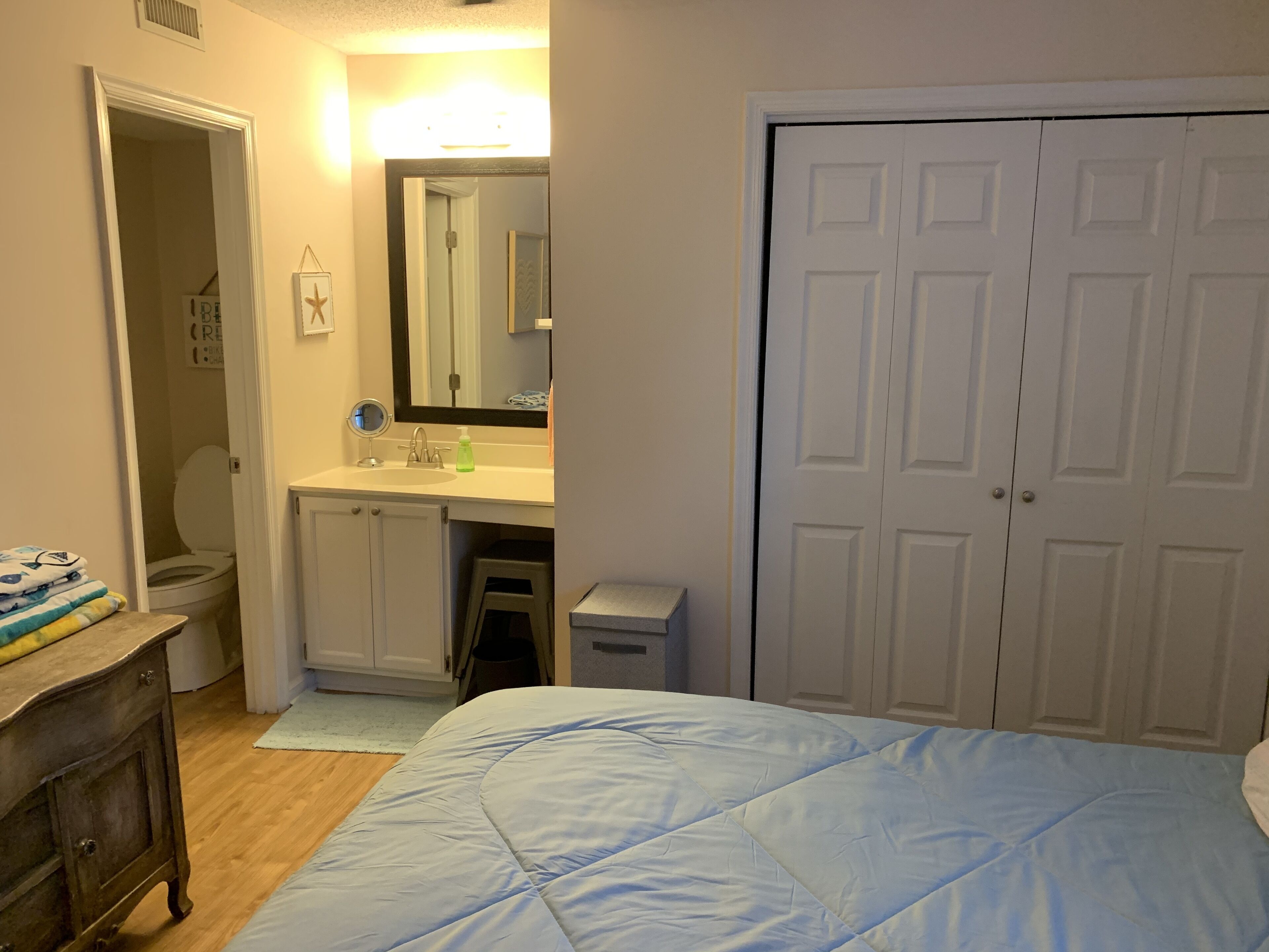 A bedroom with a bed, a dresser, a mirror, a sink, and a closet.