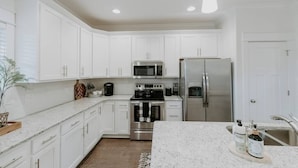 A modern kitchen with white cabinetry, stainless steel appliances, and a marble countertop.