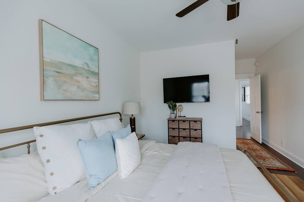 A bedroom with a bed, a TV mounted on the wall, a nightstand, and a painting.