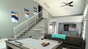 A modern living room with a pool table, a staircase, a sofa set, and a flat-screen TV. - Perfect Vegas Oasis with Gorgeous Yard/Spa and Pool, Remote Working & Vacation (Henderson)