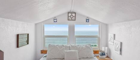 A bedroom with a bed, two windows, a wooden nightstand, and a wall-mounted shelf.