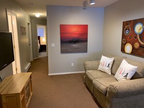 Una sala de estar con un sofá color crema, un mueble bajo de televisión de madera y un cuadro de una puesta de sol.