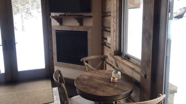 Une pièce chaleureuse avec une table et des chaises en bois, une cheminée et un téléviseur fixé au mur.