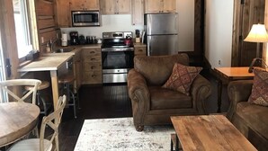 L’intérieur chaleureux d’un chalet avec des murs en bois, un coin cuisine, un canapé en cuir marron et un espace repas.